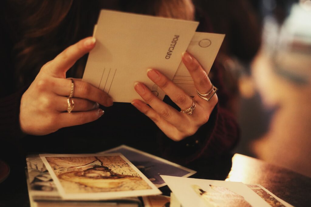 pexels-photo-36311805-36311805 Close-up of a woman holding postcards at a cozy café. Warm, intimate setting.